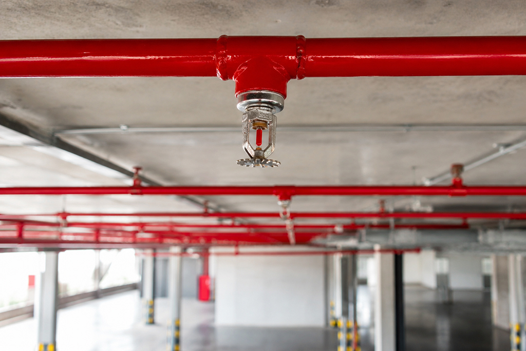 Red fire sprinkler head connected to a commercial piping system installed on a concrete ceiling.